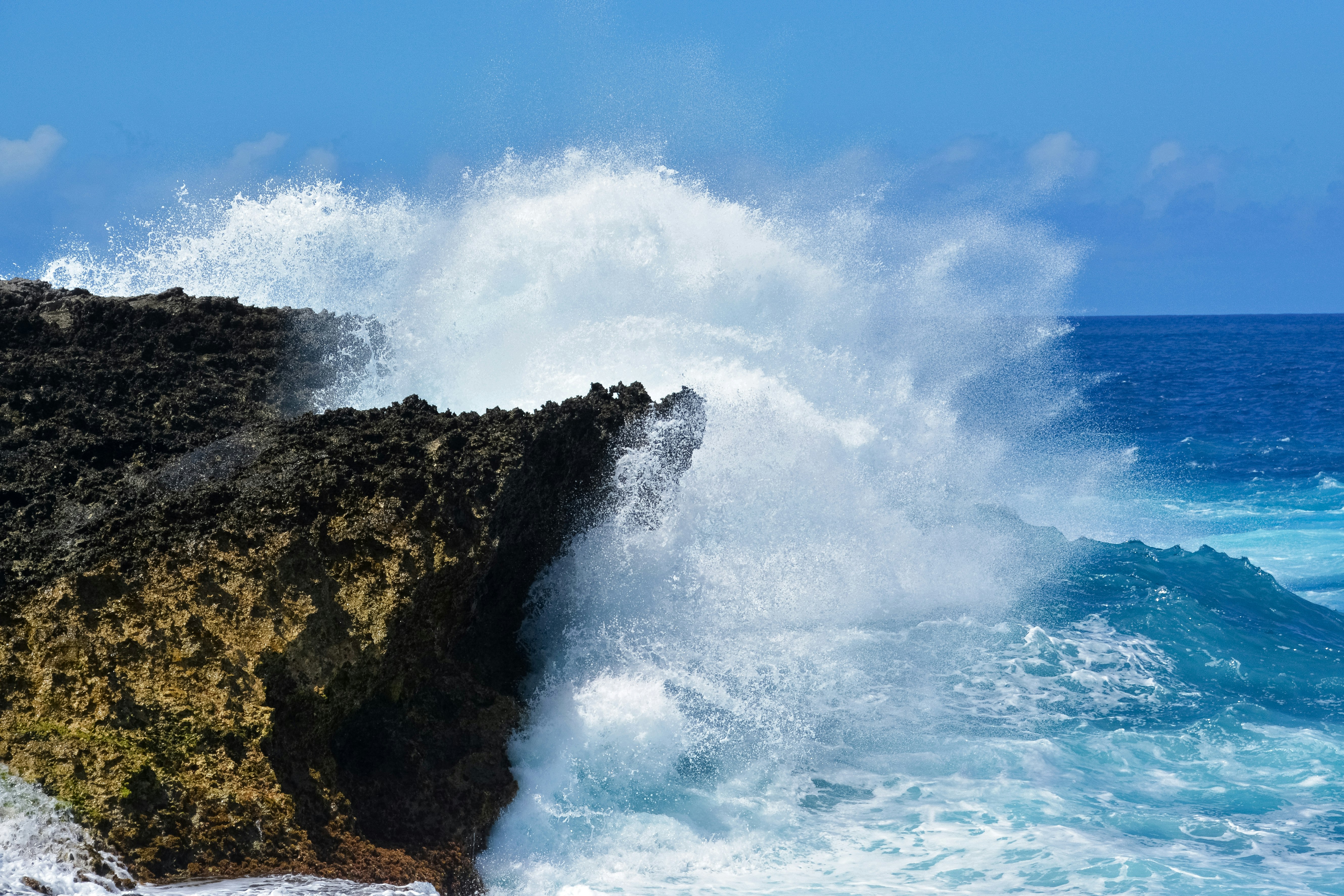 ocean waves crashing on brown rock formation under blue sky during daytime